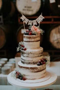 a three tiered wedding cake with berries and flowers on top sits in front of wine barrels