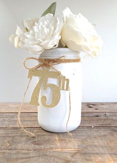 white flowers in a mason jar with the number seventy on it's string tied around the top