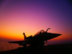 a fighter jet sitting on top of an aircraft carrier under a purple and orange sky