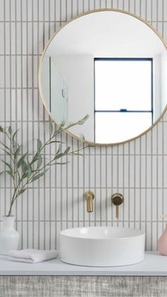 a white sink sitting under a round mirror next to a vase with a plant in it