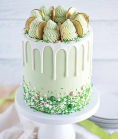 a white cake with green frosting and gold cookies on top is sitting on a plate