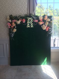 a green backdrop with flowers on it in front of a window, and a bow at the top