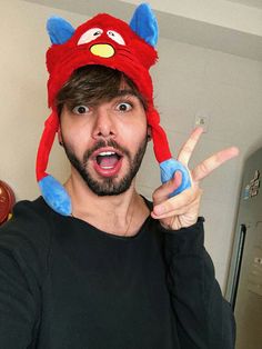 a man wearing a red and blue animal hat making the peace sign with his fingers