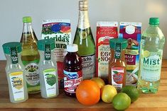 an assortment of condiments and beverages on a wooden counter top, including oranges, lemons, limes, water, juice, and more