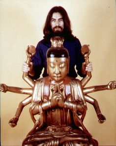 a man sitting on top of a wooden statue next to a golden buddha figure with arms outstretched