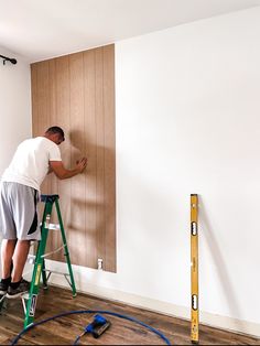 a man on a ladder painting a wall with wood paneling and paint rollers