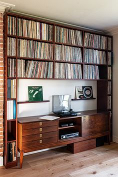 a record player is sitting on top of a wooden shelf in front of a bookshelf filled with records