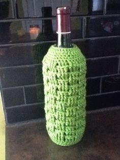 a green crocheted bottle cover sitting on top of a counter next to a brick wall