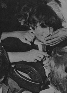 black and white photograph of young boy holding hat with other people around him looking at it