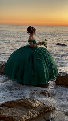 a woman in a green dress is sitting on rocks by the ocean at sunset or dawn