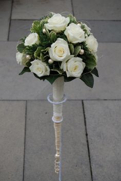 a bouquet of white roses and greenery on a stand