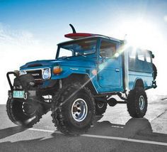 a large blue truck parked in a parking lot next to the ocean on a sunny day