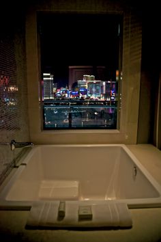 a bath tub sitting next to a window with a view of the city at night