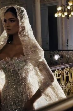 a woman in a white wedding gown and veil standing next to a stair case with chandeliers on it