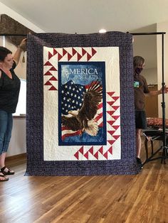 two women holding up a quilt with an american flag and eagle on it, while another woman stands in the background