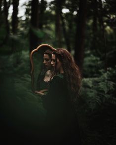 a man and woman standing in the woods looking at each other's faces with long hair