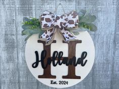 a wooden ornament with the word h on it and a cow print bow