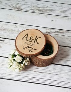 a wooden ring box with the initials and wedding date on it sitting next to flowers