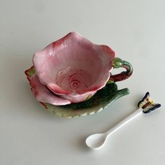 a pink flower sitting on top of a plate next to a spoon