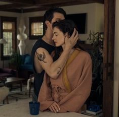 a man and woman standing next to each other in a living room with a coffee cup