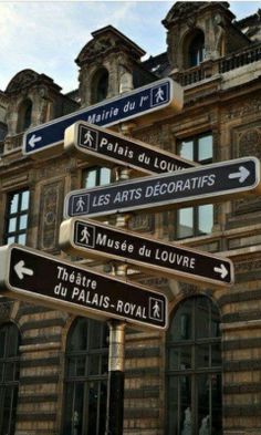 a street sign in front of a building with many windows and signs pointing to different locations