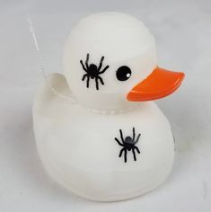 a white rubber duck with orange beak and spider legs on it's head, sitting in front of a white background