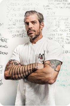 a man with his arms crossed standing in front of a whiteboard covered with writing