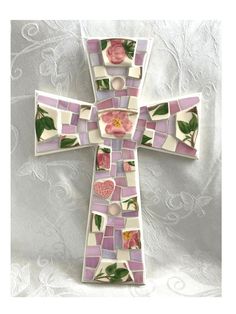 a cross made out of tiles with flowers on the front and sides, sitting on top of a white cloth