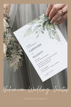 a person holding a wedding card in their hand with flowers and greenery on it