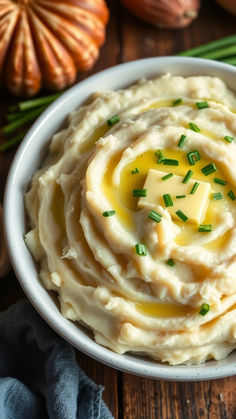 a white bowl filled with mashed potatoes topped with butter and chives on top of a wooden table