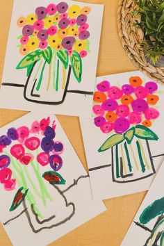 four cards with flowers in vases on them sitting next to a basket of grass