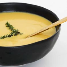 a black bowl filled with yellow soup and a wooden spoon in the bowl next to it