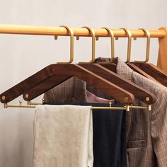 clothes hanging on wooden hangers in front of a white wall and coat rack with folded shirts