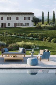 an outdoor living area with couches and tables next to a swimming pool in front of a large house