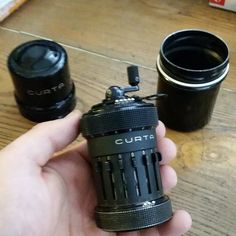 a person holding a camera lens in their left hand and two cups on the other