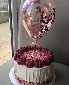 a birthday cake decorated with pink and purple icing, topped with a large balloon