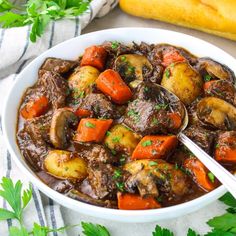 a white bowl filled with stew and carrots on top of a table next to bread