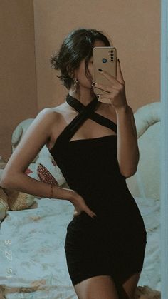 a woman in a black dress taking a selfie with her cell phone while standing on a bed