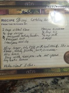 a recipe board with writing on it in front of a granite counter top and an old penny