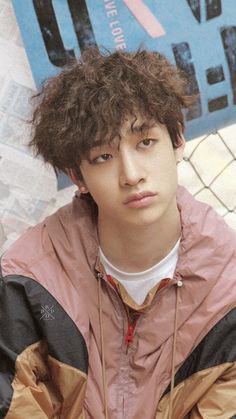 a young man with curly hair wearing a pink and black jacket looking at the camera