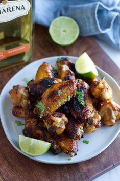 a white plate topped with chicken wings and garnished with limes next to a bottle of gin