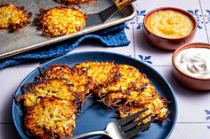 a blue plate topped with crab cakes next to two bowls of dips and a fork