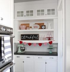 a kitchen with white cabinets, black counter tops and red decorations on the shelf above it