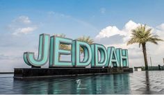 a large sign that says jeddah in front of palm trees