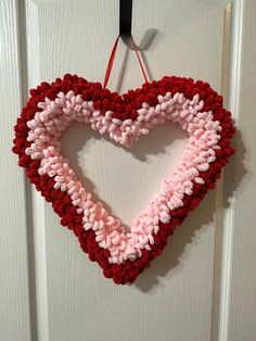 a crocheted heart hanging on a door with red, pink and white yarn