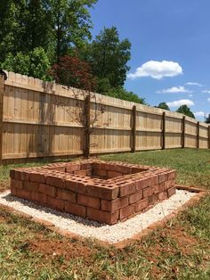 a brick fire pit sitting in the middle of a yard next to a wooden fence