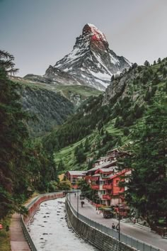 a river running through a lush green forest covered hillside next to a tall snow capped mountain