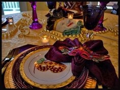 the table is set with purple and gold plates, napkins, and candle holders