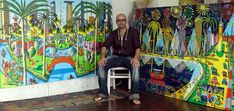 a man sitting on a chair in front of some colorful art work with palm trees