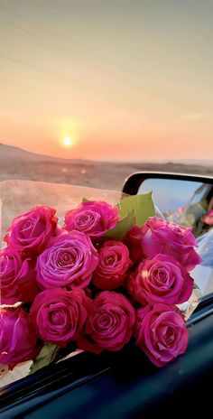 a bouquet of pink roses sitting on the hood of a car with the sun setting in the background